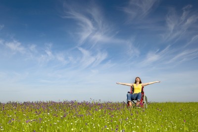 joyful woman using wheelchair in field of flowers