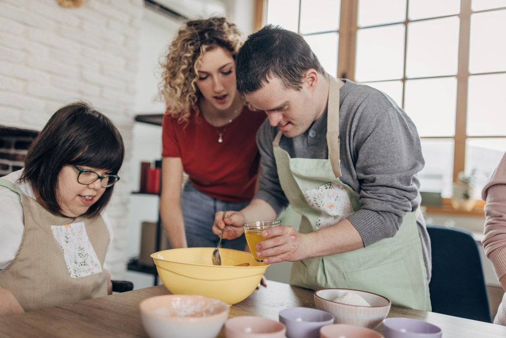 Group of people, men and women with down syndrome on cooking class, there is teacher with them.