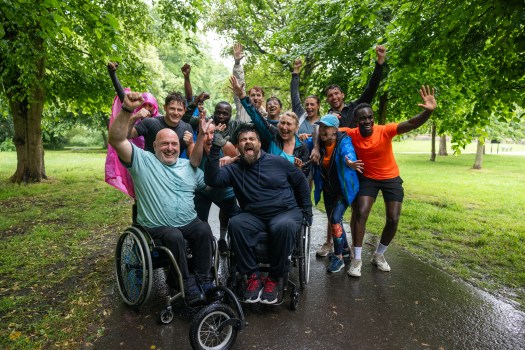 A group of individuals, some utilizing wheelchairs, are all looking into the camera with a cheerful look on their faces.