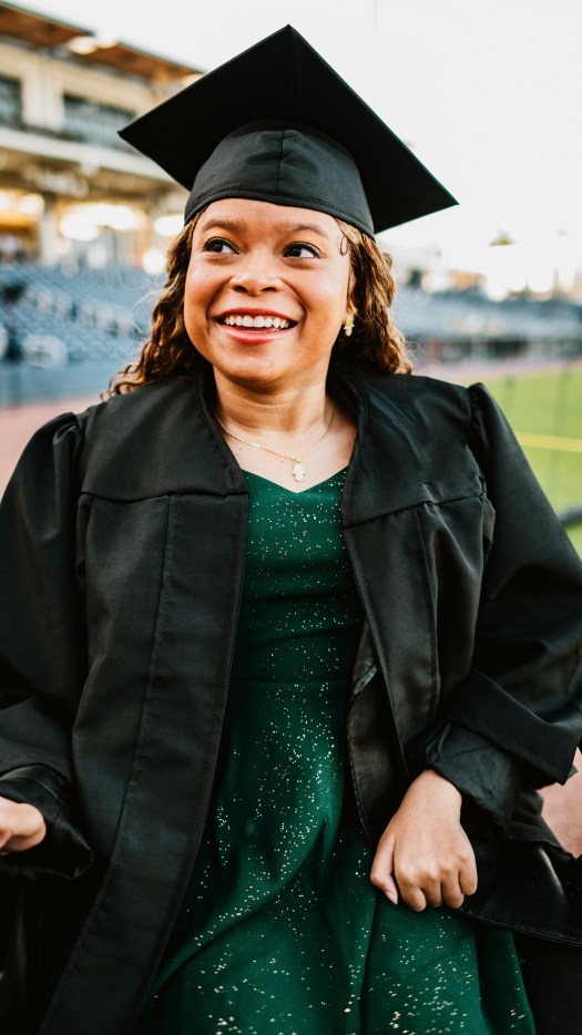 Woman utilizing a power wheelchair is dressed in graduation cap & gown
